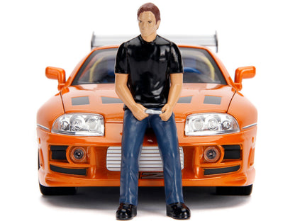 Model figure of a person standing in front of an orange car on a white background