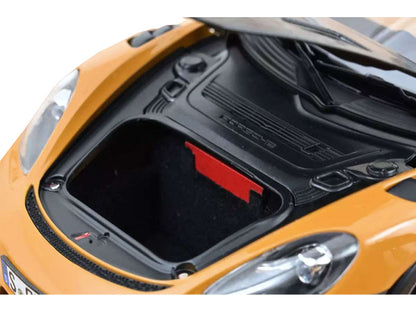 Close-up of a car's open hood with a red label on an orange car.