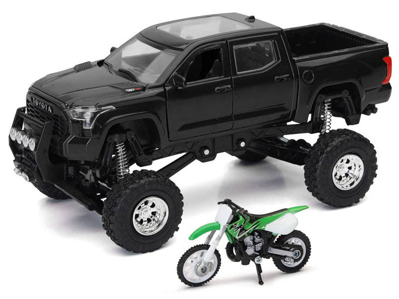 Black toy truck with large wheels and a green and white toy dirt bike on a white background
