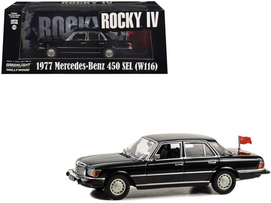 A 1/43 scale diecast model of a 1977 Mercedes-Benz 450 SEL (W116) in black color with a Soviet flag, representing the movie 'Rocky IV'. The model features chrome accents and real rubber tires.