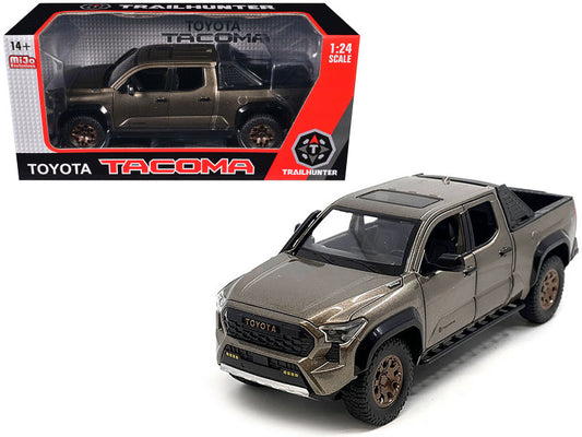 A diecast model of a 2024 Toyota Tacoma Trailhunter Edition Pickup Truck in bronze metallic color, with details such as real rubber tires, posable wheels, and a removable tire and roof rack.