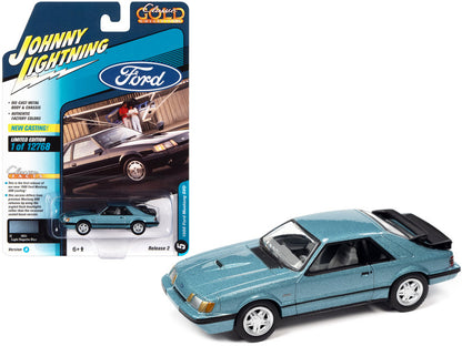 A 1/64 scale die cast model of a 1986 Ford Mustang SVO in Light Regatta Blue Metallic with black stripes, packaged in a blister pack with 'Johnny Lightning' branding.