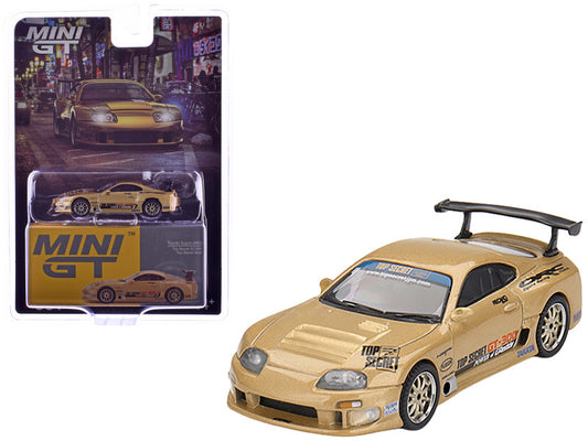 Gold toy car with black spoiler next to its packaging on a white background