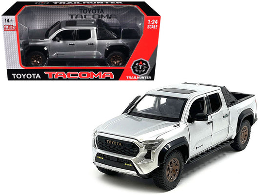 A diecast model of a 2024 Toyota Tacoma Trailhunter Edition Pickup Truck in silver color, showing the model with detailed interior, exterior, and real rubber tires.
