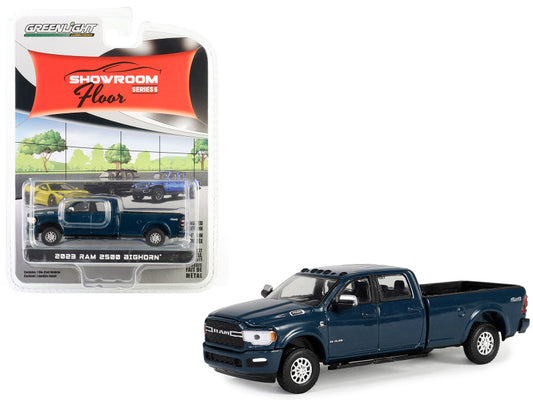 A diecast model of a 2023 Dodge Ram 2500 Bighorn Pickup Truck in Patriot Blue Metallic color, packaged in a blister pack with a 'Showroom Floor' series label.