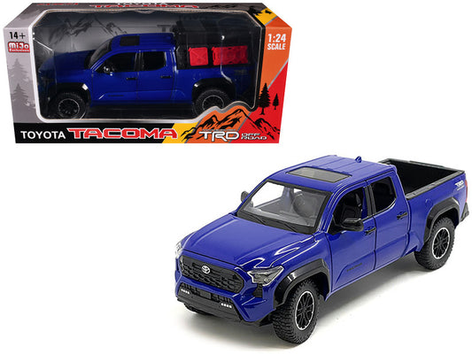 A diecast model of a blue 2024 Toyota Tacoma TRD Off-Road Edition Pickup Truck with a bed camper, displayed in its packaging.